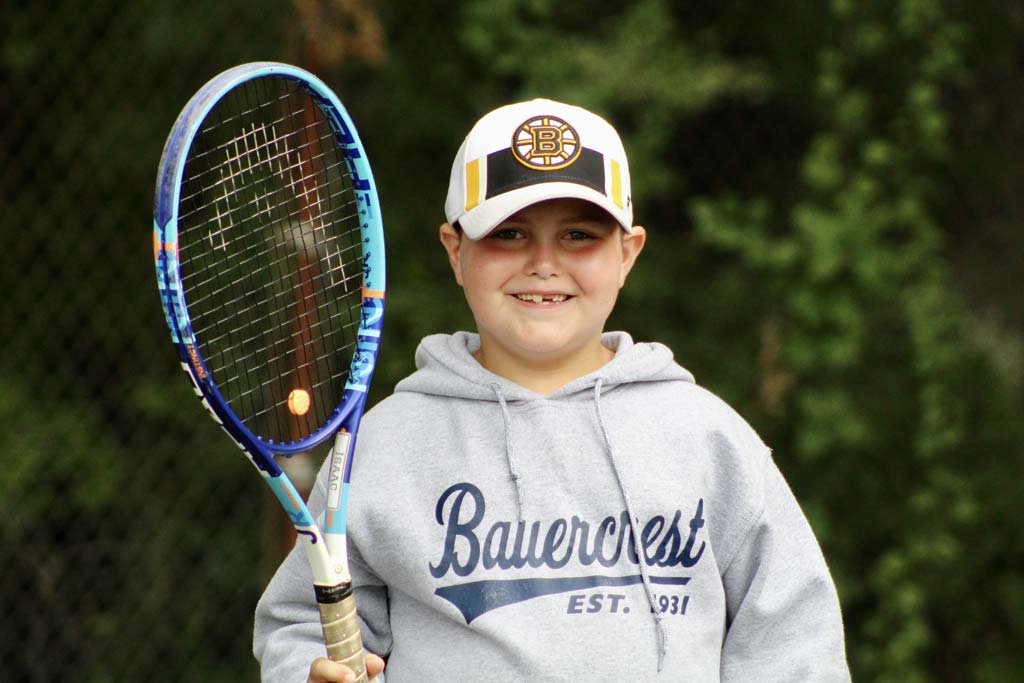 Young camper with tennis racquet smiling