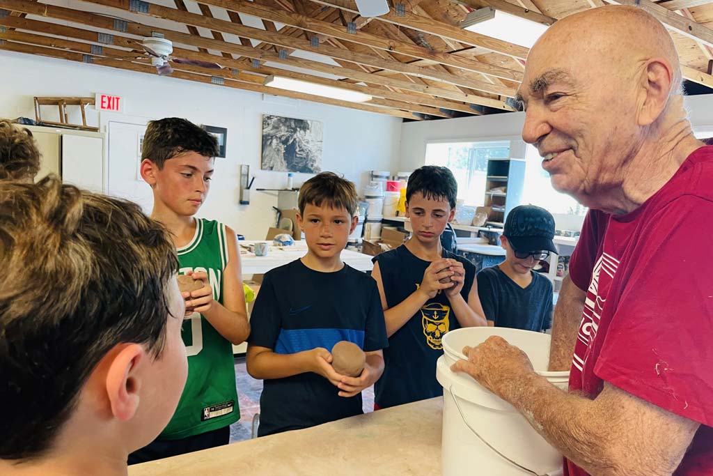 Elderly teacher works with campers and a ceramics project